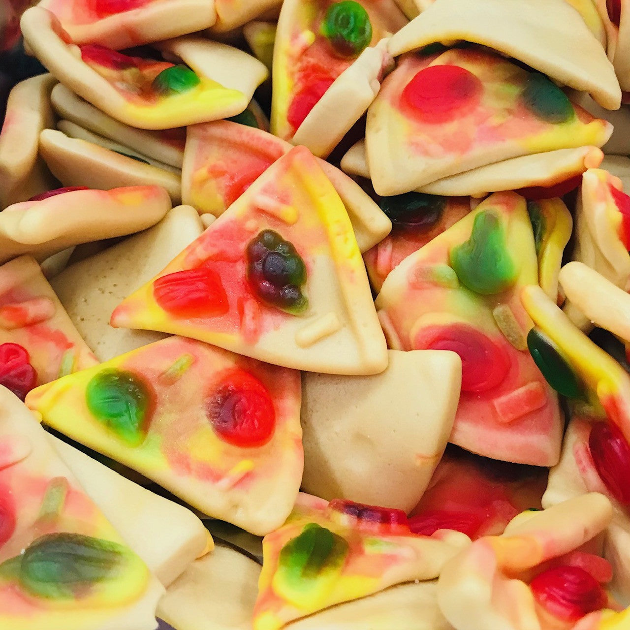 Gummy pizza slice candies with realistic pizza appearance featuring triangular slices with colorful fruit gummy toppings resembling pepperoni, peppers, and other pizza ingredients on a cheese-colored base
