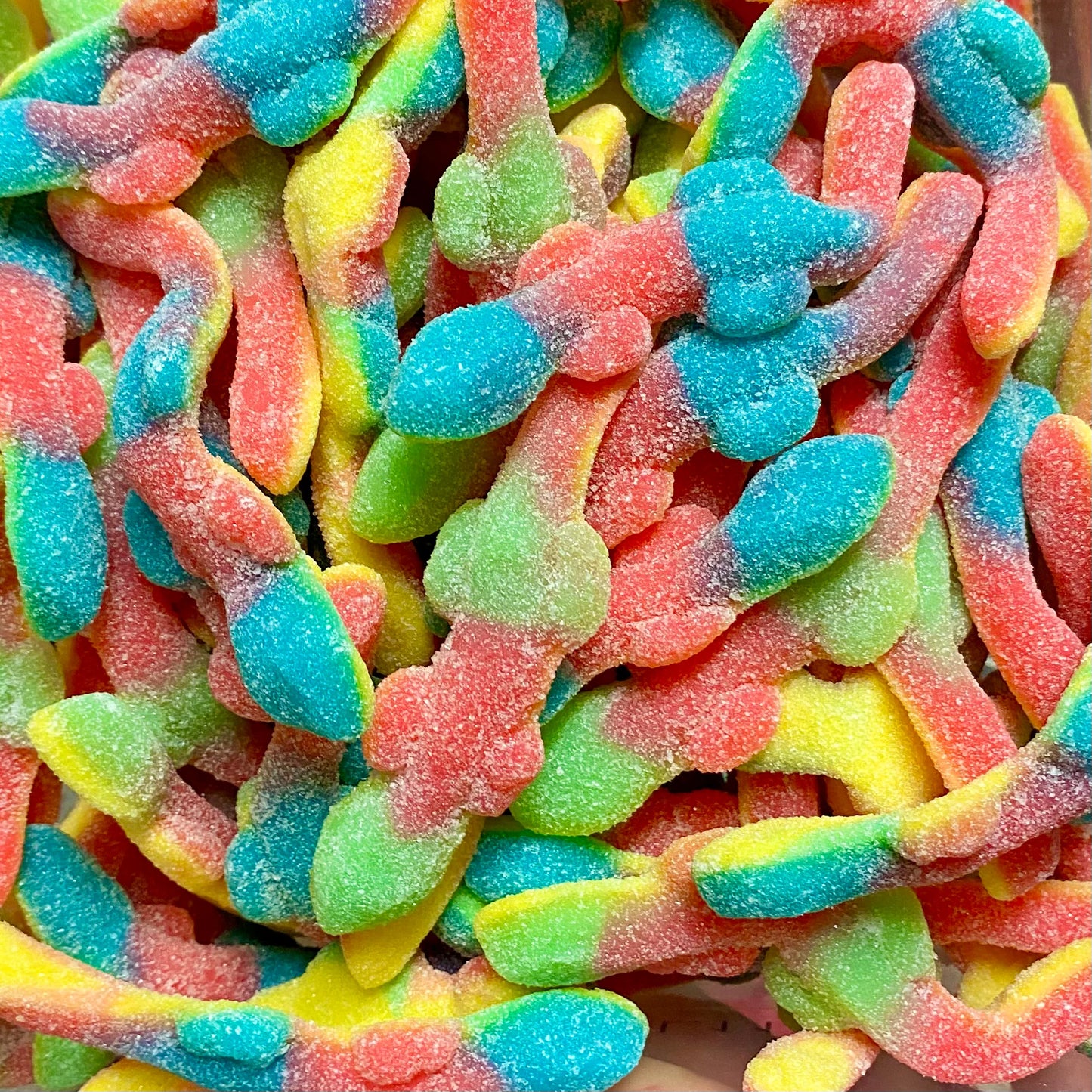 Colorful sour lizard-shaped gummy candies in red, blue, green, and yellow covered in sugar crystals, showing reptile shapes with detailed lizard forms