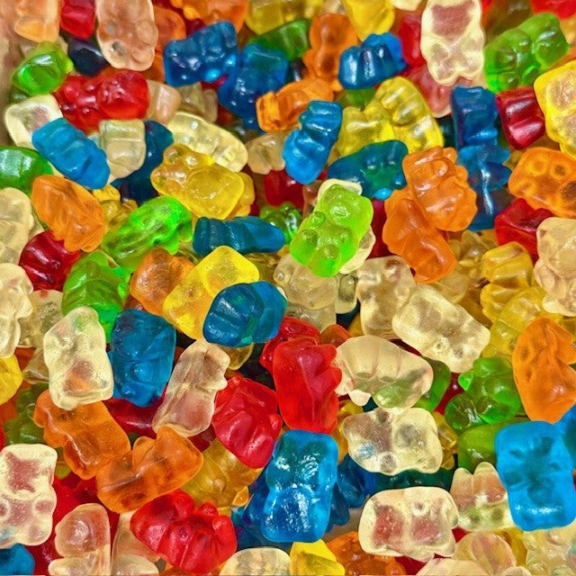 Colorful gummy bears in assorted flavors including red, blue, green, yellow, orange, and clear with glossy finish, showing classic bear shapes scattered across the frame
