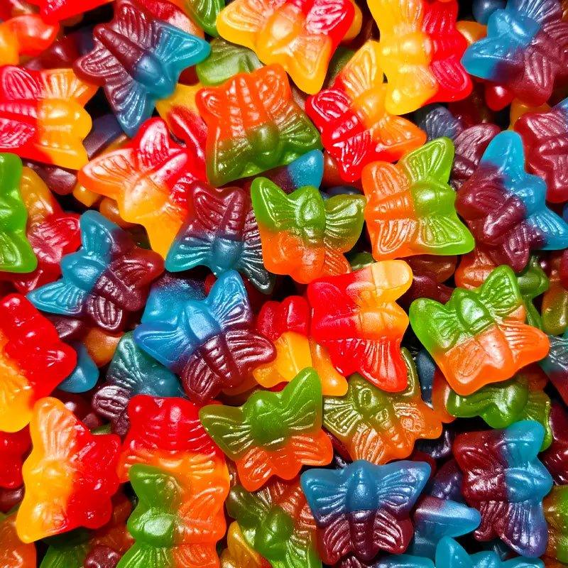 Colorful gummy butterfly candies in vibrant shades of red, orange, yellow, green, blue, and purple with detailed wing patterns and textures scattered across the frame