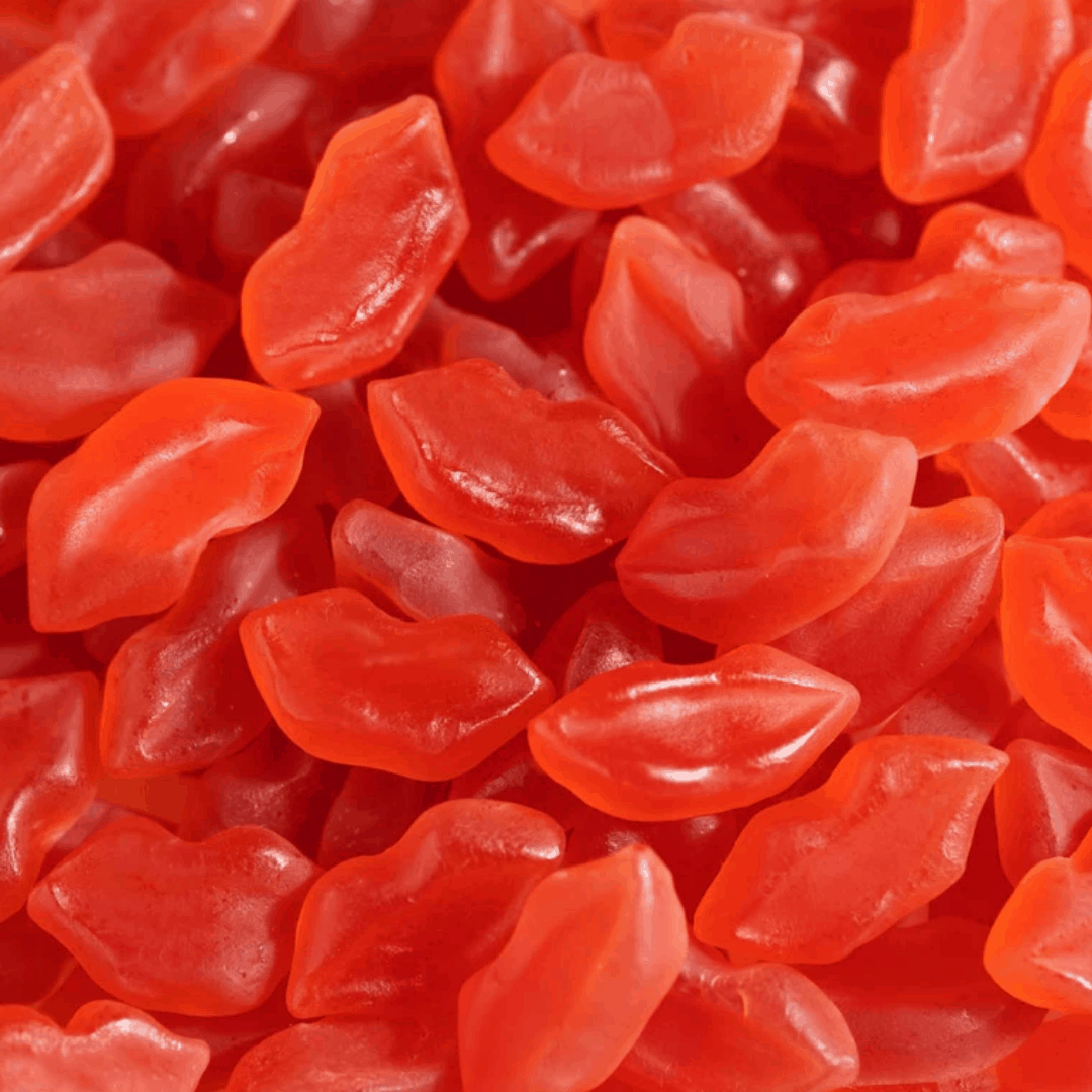 Red gummy lips candy in realistic lip shapes with glossy finish, showing kiss-shaped confectionery treats scattered across the frame
