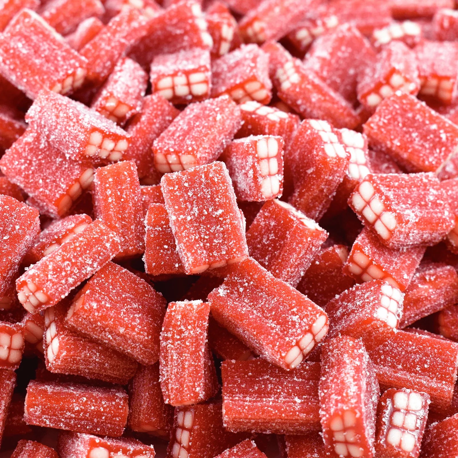 Red strawberry brick-shaped gummy candies with white textured details resembling brick patterns, covered in sugar crystals and scattered across the frame