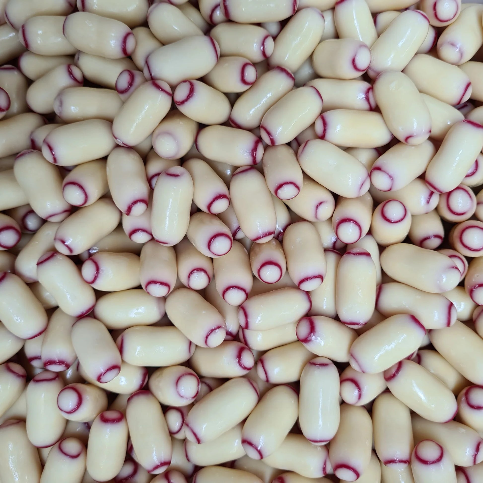 lose-up view of white chocolate bullet candies with purple raspberry swirl patterns scattered across the frame, showing their oval bullet shape and creamy white surface with decorative purple markings